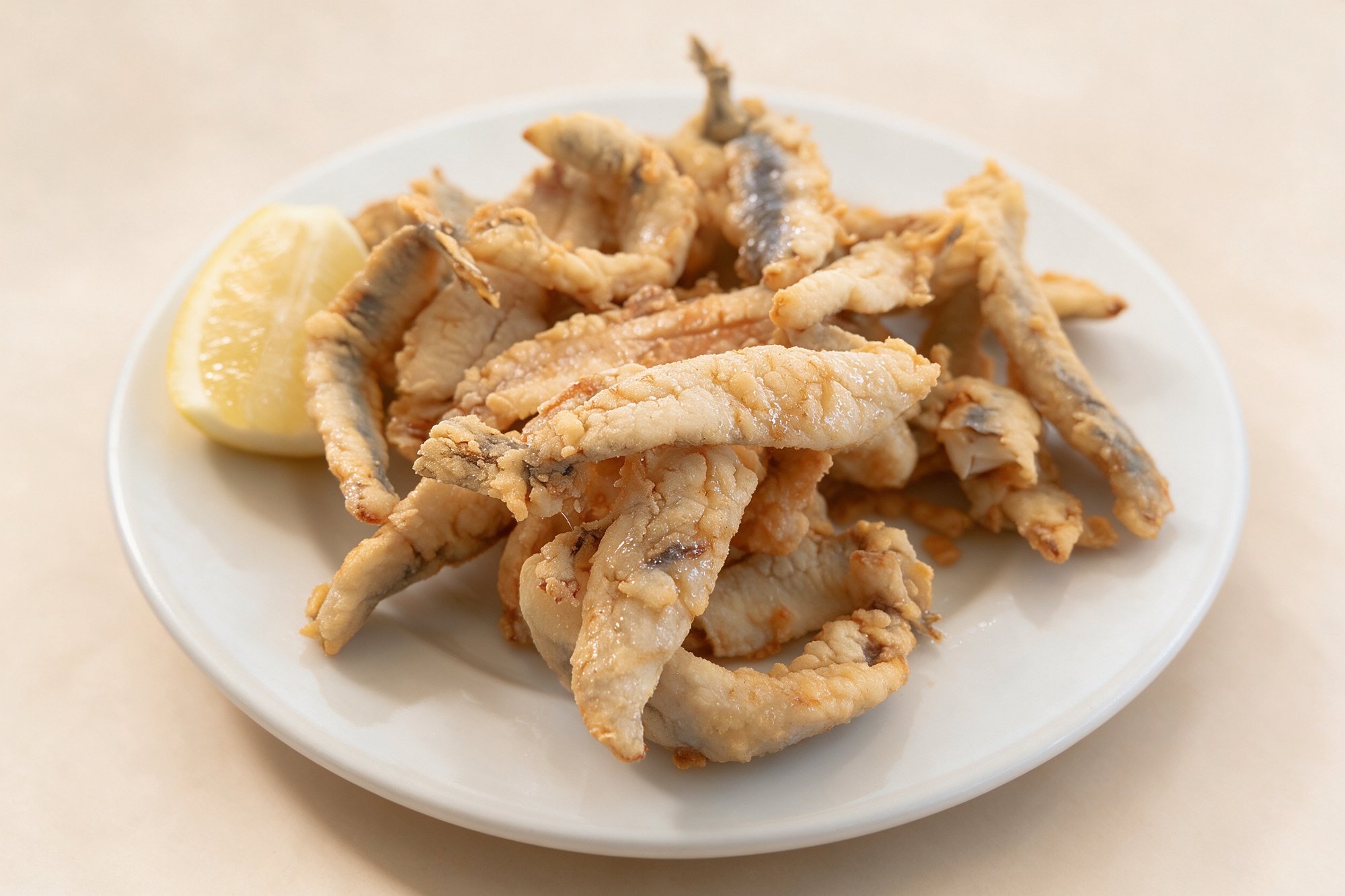 Pescaditos Fritos de Bar Los Pescadores, pequeños pescados rebozados y crujientes en plato blanco con limón